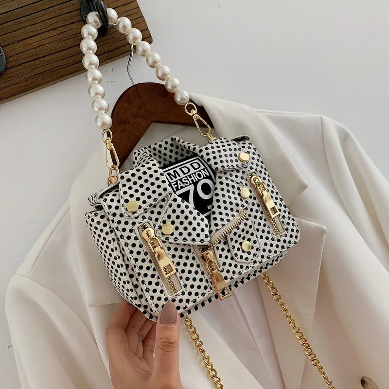 Polka dot handbag with gold chain and pearl strap held by a hand on a white background