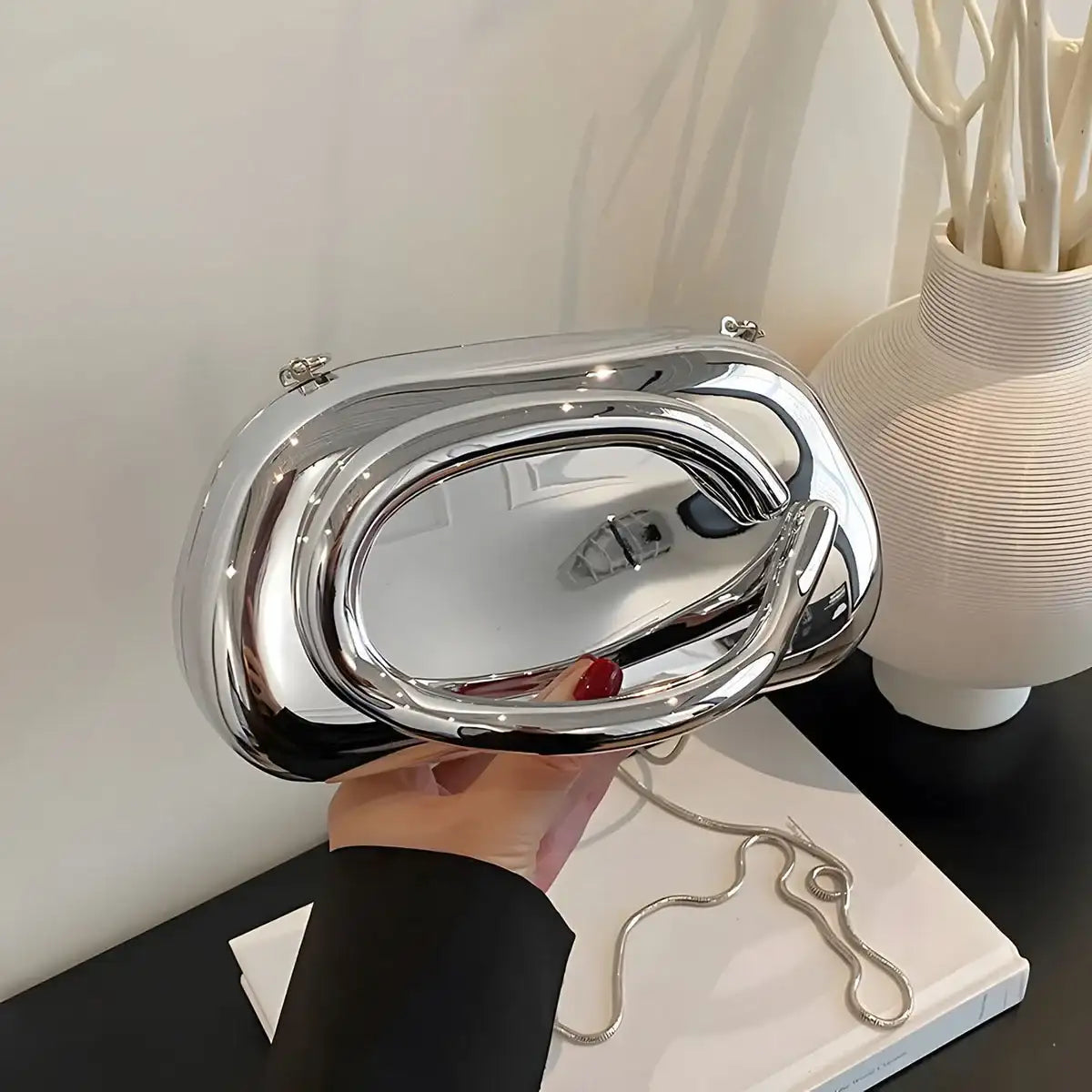 Silver Metallic Carauana Festival Clutch Bag held by a hand on a light background