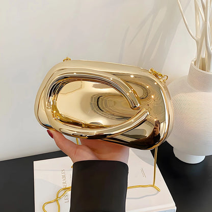 Gold clutch held by a hand on a white surface with a lamp and vase in the background