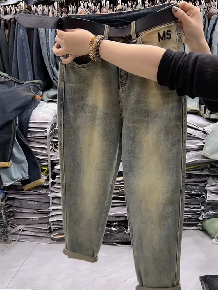 Person holding up a pair of distressed jeans with 'MS' branding in a clothing store.