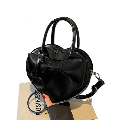 Black handbag with a bow detail held by a hand on a white background