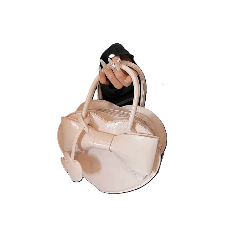 Beige handbag with bow detail held by a hand against a white background