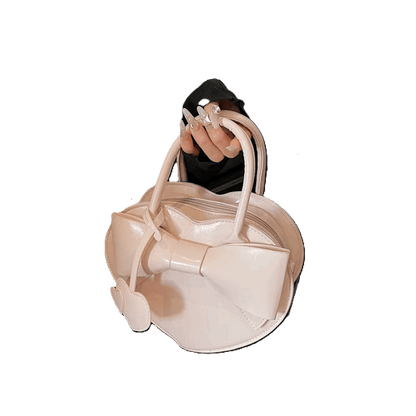 Beige handbag with bow detail held by a hand against a white background